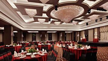 A banquet hall with round tables, red tablecloths, and black chairs.