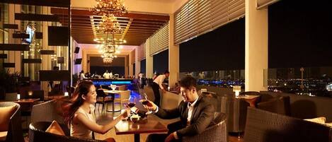 Eine moderne Lounge mit Korbmöbeln, einer Bar im Hintergrund und Blick auf die Stadt durch große Fenster.