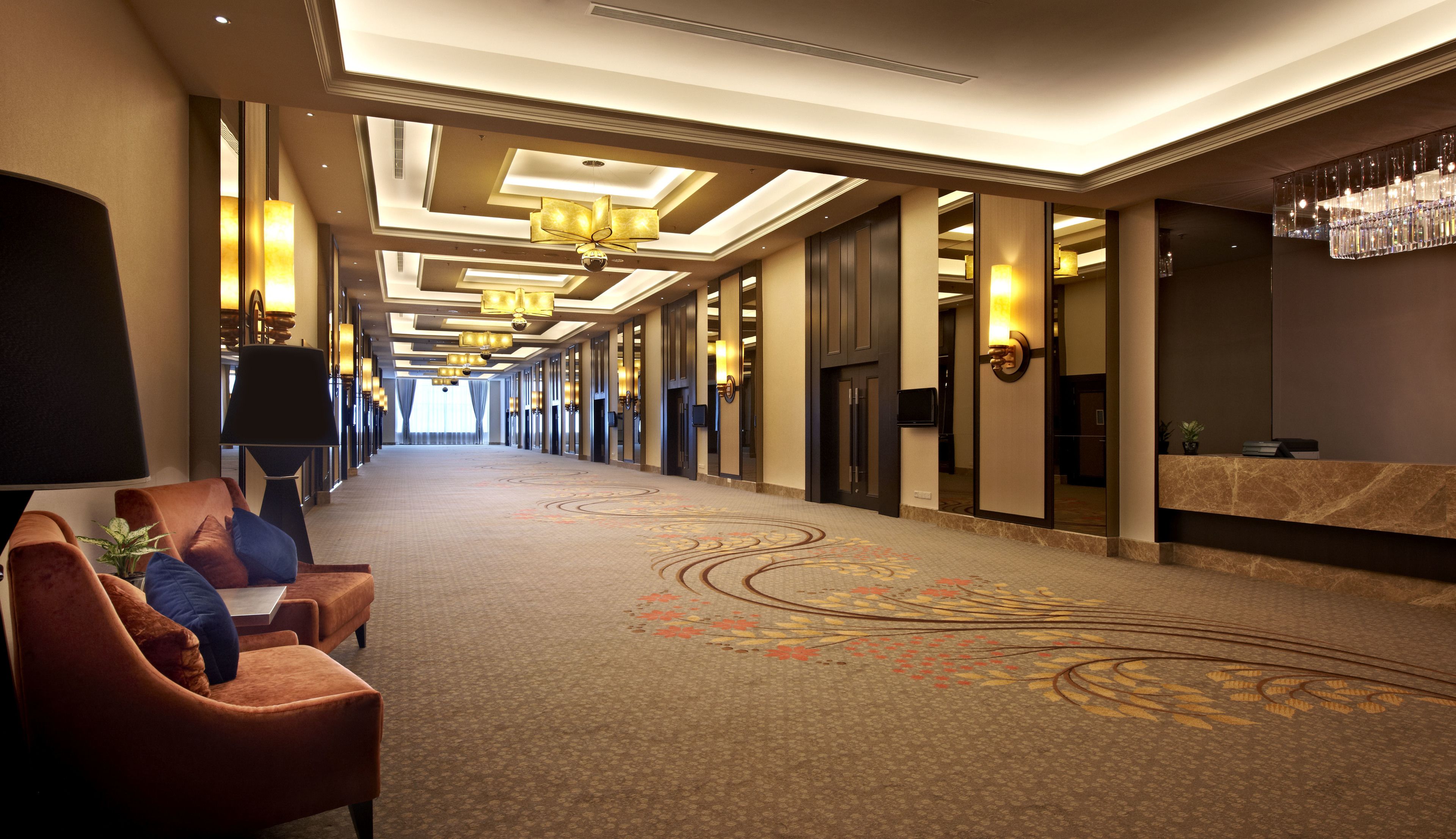 A hotel corridor with a carpeted floor, seating area with chairs, and a reception desk.