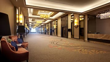 A hotel corridor with a carpeted floor, seating area with chairs, and a reception desk.