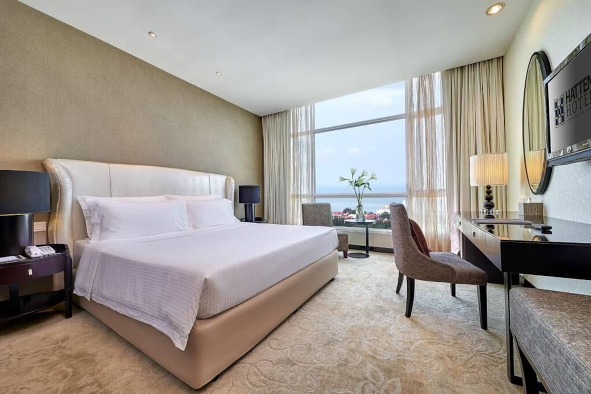 Ein Hotelzimmer mit einem großen Bett, einem Schreibtisch, einem Sessel und Blick auf die Stadt.