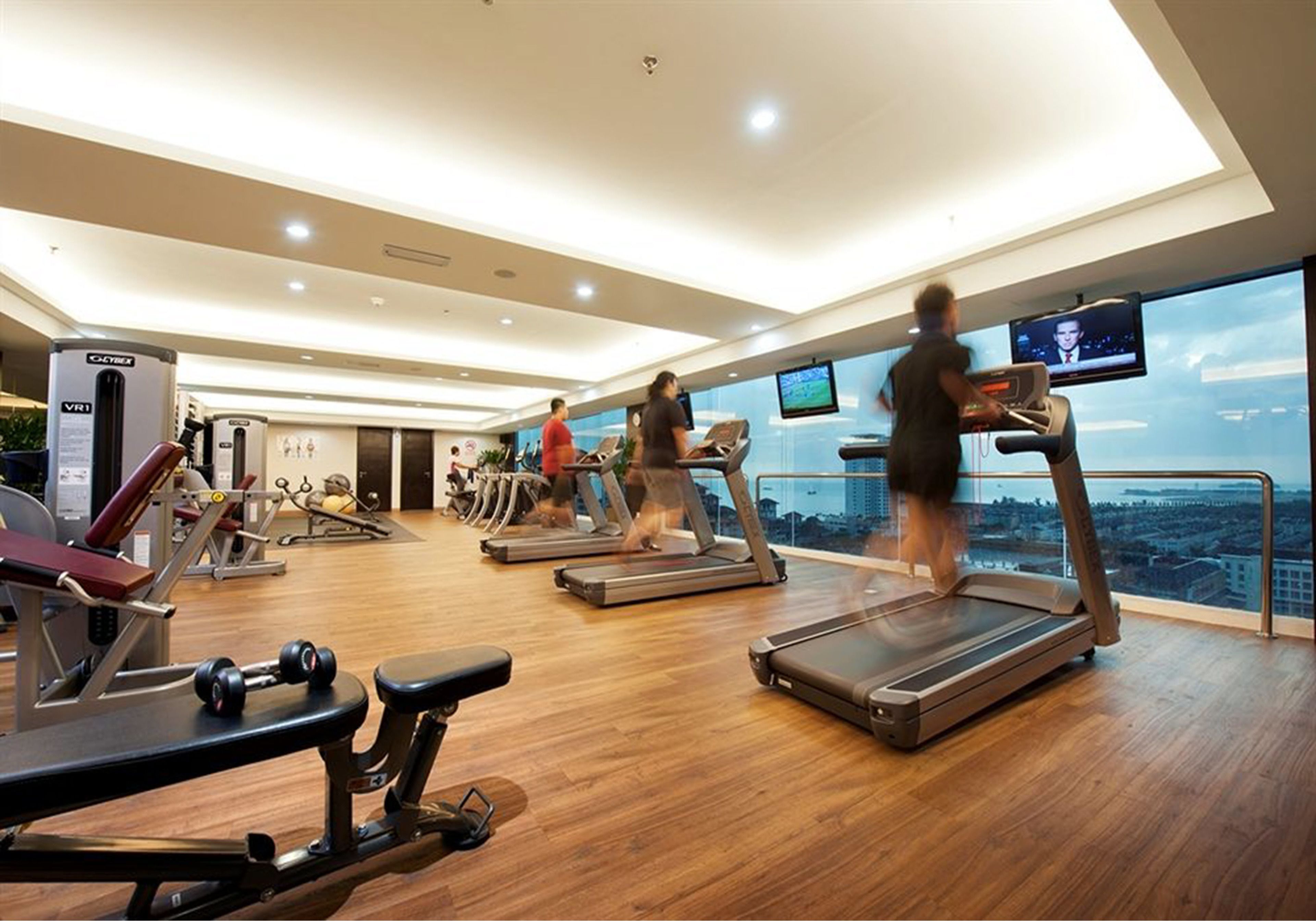 A gym with treadmills, weight machines, and a large window overlooking a cityscape.