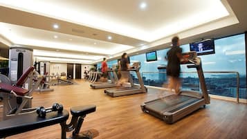 A gym with treadmills, weight machines, and a large window overlooking a cityscape.