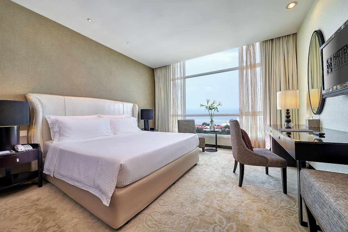 Ein Hotelzimmer mit einem großen Bett, einem Schreibtisch, einem Stuhl und Blick aufs Meer.