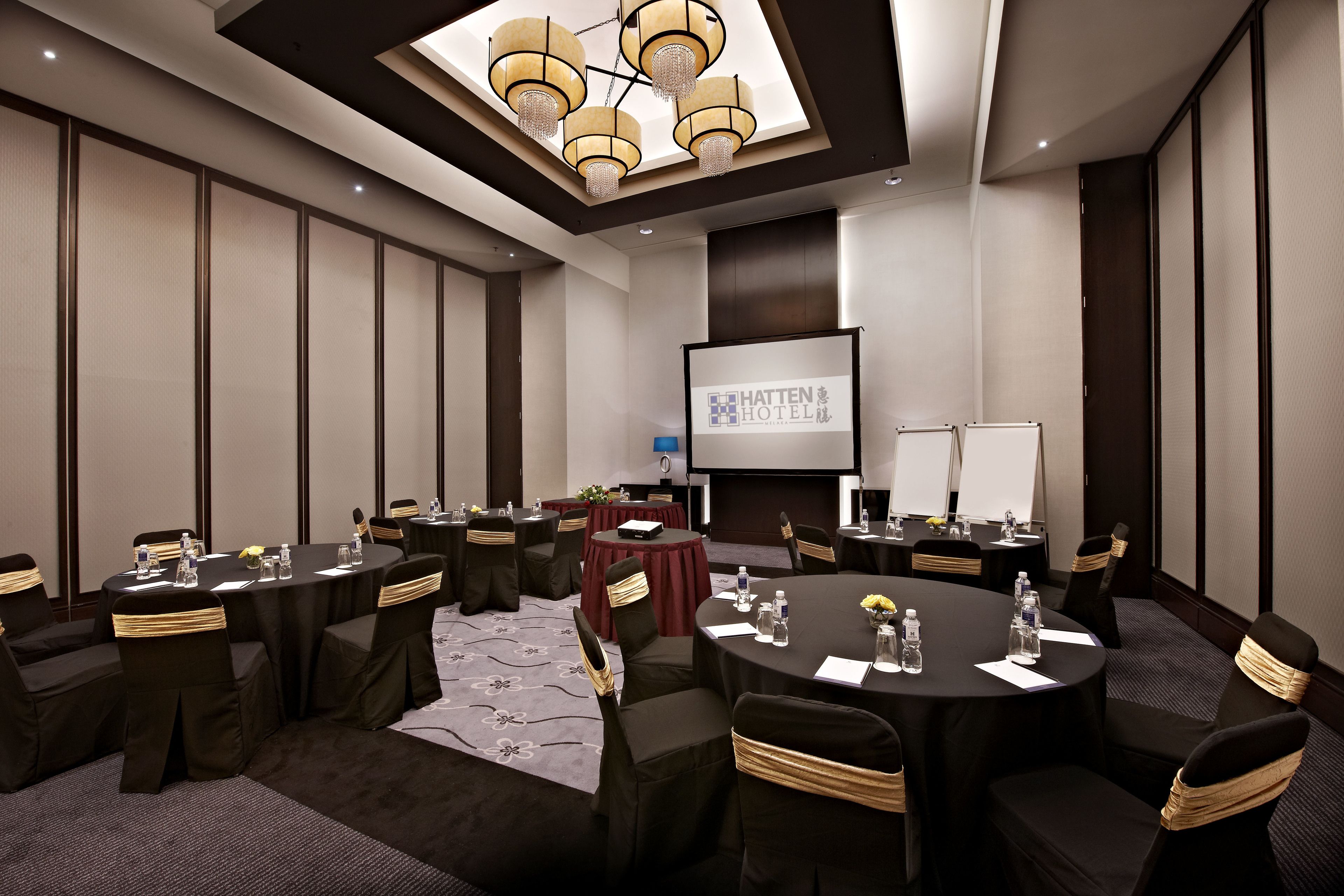 Ein Konferenzraum mit runden Tischen, Stühlen und einer Projektionsleinwand, die den Namen des Hotels zeigt.