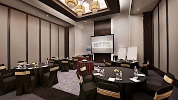 Ein Konferenzraum mit runden Tischen, Stühlen und einer Projektionsleinwand, die den Namen des Hotels zeigt.