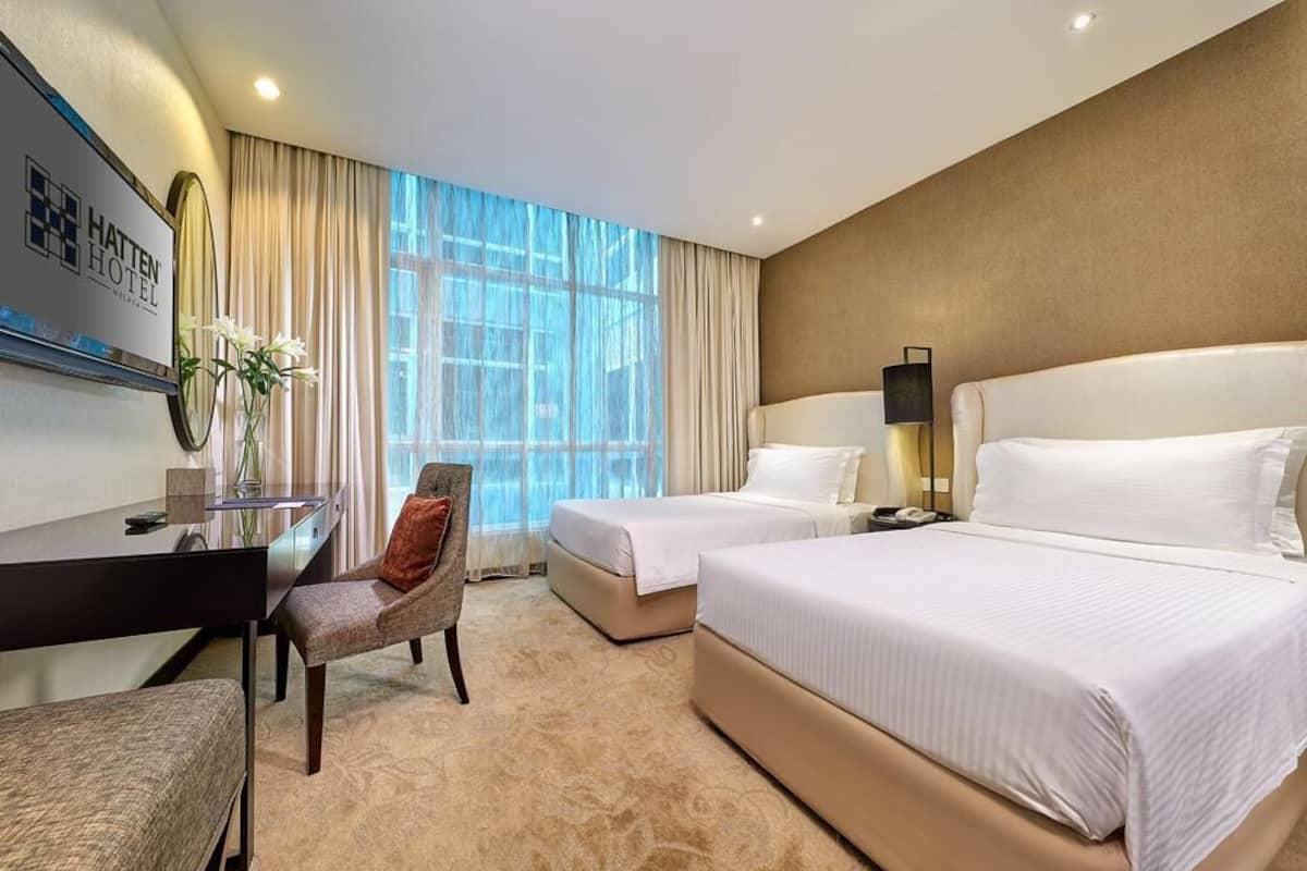 Ein Hotelzimmer mit zwei Betten, einem Schreibtisch, einem Stuhl und einem großen Fenster mit Vorhängen.