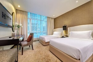 Habitación de hotel con dos camas, un escritorio, una silla y un ventanal con cortinas.