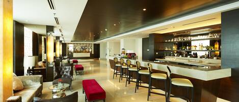 Un hall d’hôtel moderne comprenant un bar, des espaces de détente et un comptoir d’accueil.