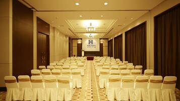 A hotel conference room with rows of white chairs and a stage at the front.