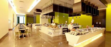 A modern hotel lobby with a central food display, seating area, and a staircase.