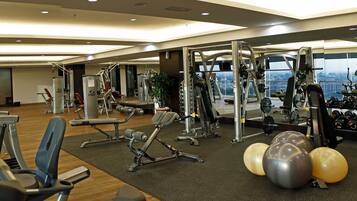 A modern gym with various exercise equipment, a mirror, and a view of the city through large windows.