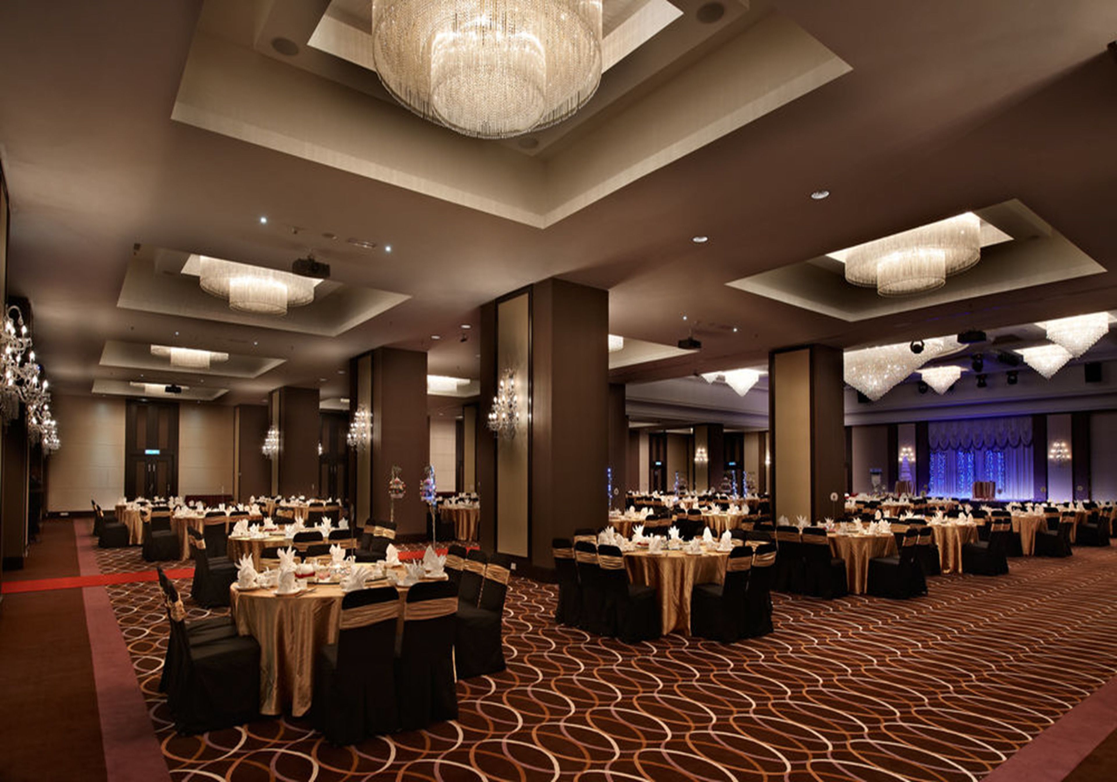 A banquet hall with round tables, chandeliers, and a patterned carpet.