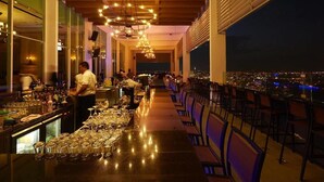 Un restaurante con una barra larga, varias mesas y vistas a la ciudad.