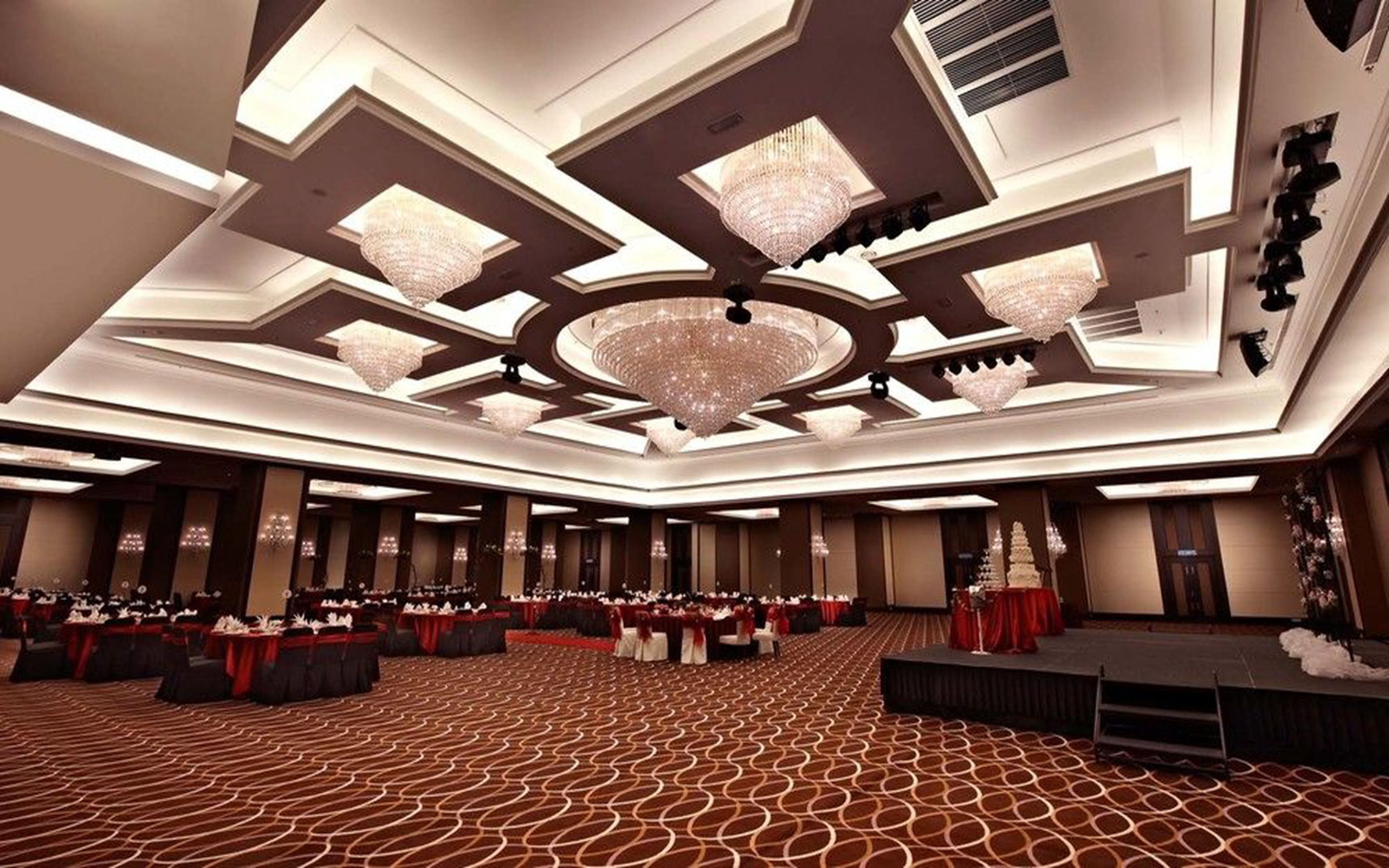 A spacious banquet hall with a high ceiling, multiple chandeliers, and rows of tables set for events.