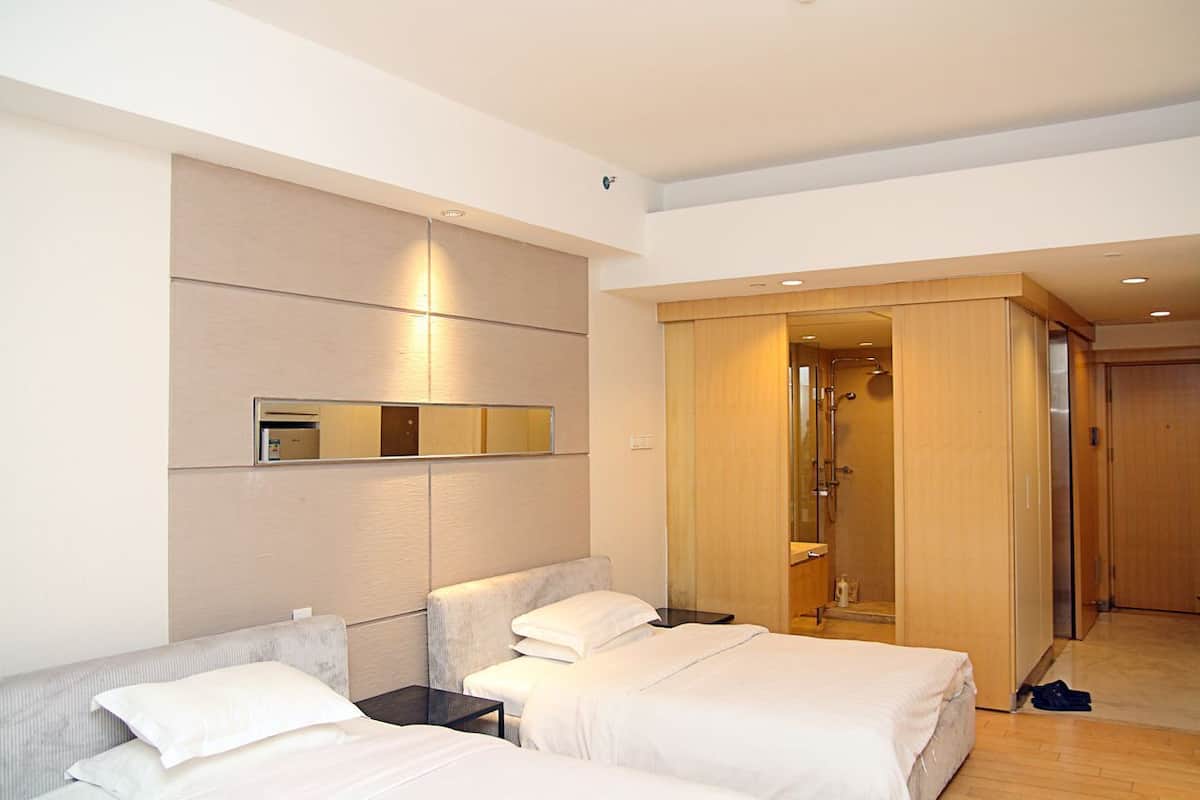 A hotel room with two beds, a large mirror, a walk-in closet, and a shower area.