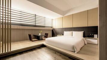 A modern bedroom with a large bed, bedside tables, a desk, and a window with blinds.