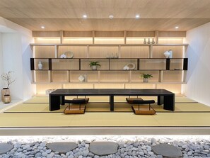 A modern interior with a long dark wooden table, multiple shelves with decorative items, and a stone-tiled floor. - Suye Hotel (Taichung)