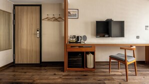 A hotel room with a wooden floor, a desk with a chair, a television, and a wardrobe. - Suye Hotel (Taichung)
