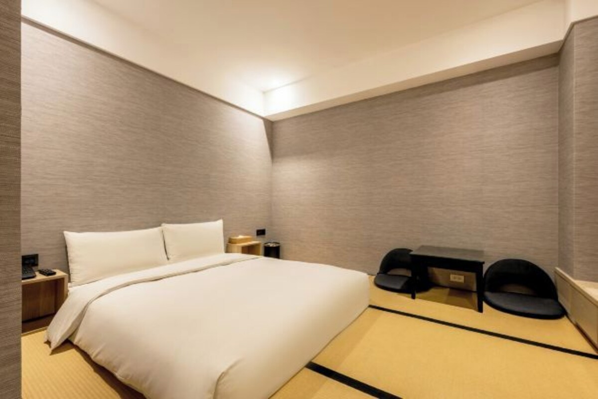A modern hotel room with a large bed, a small desk, and a chair.