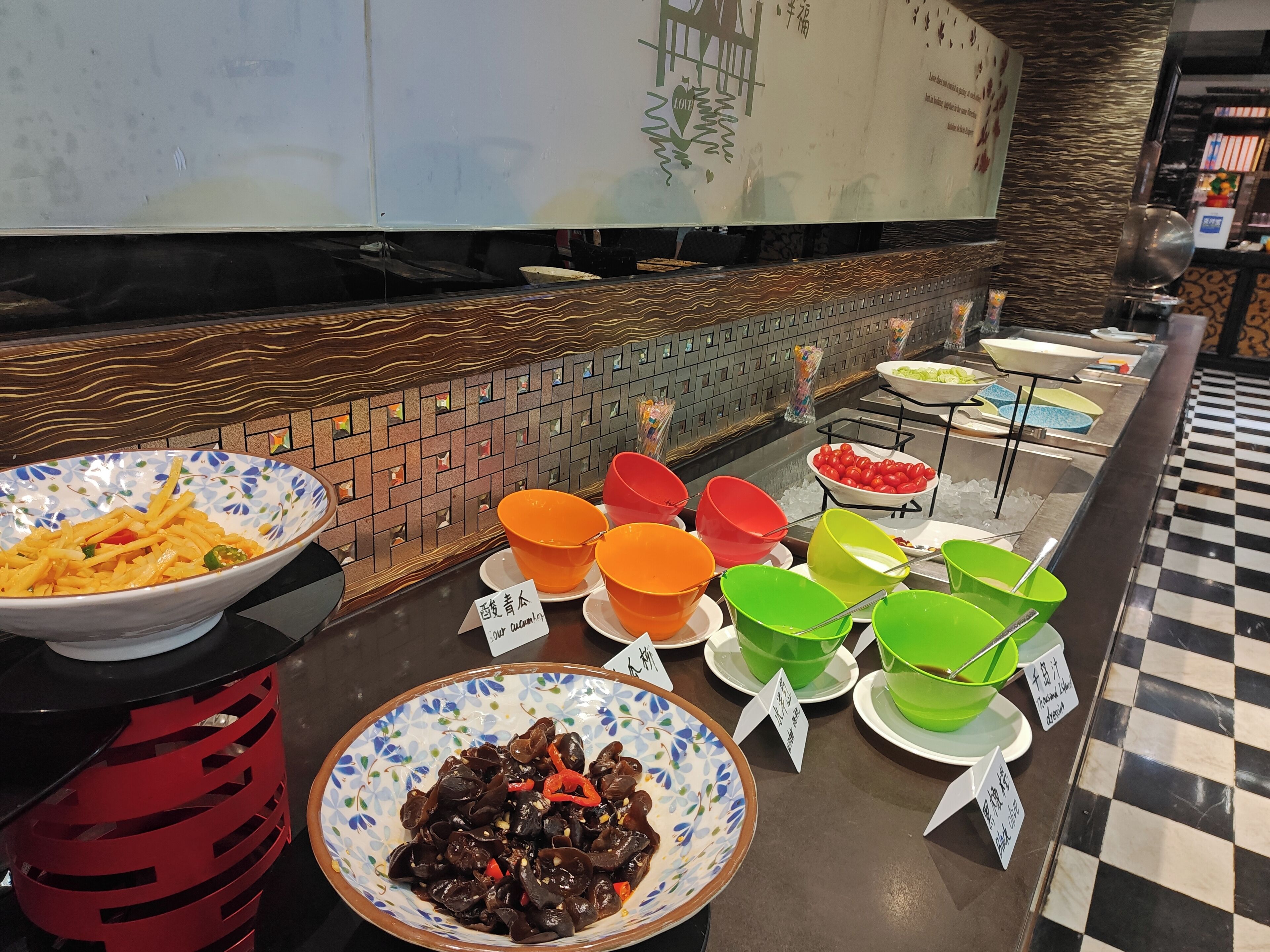 Un buffet proposant divers plats présentés dans des bols colorés, un mur recouvert de carreaux et un sol à carreaux.