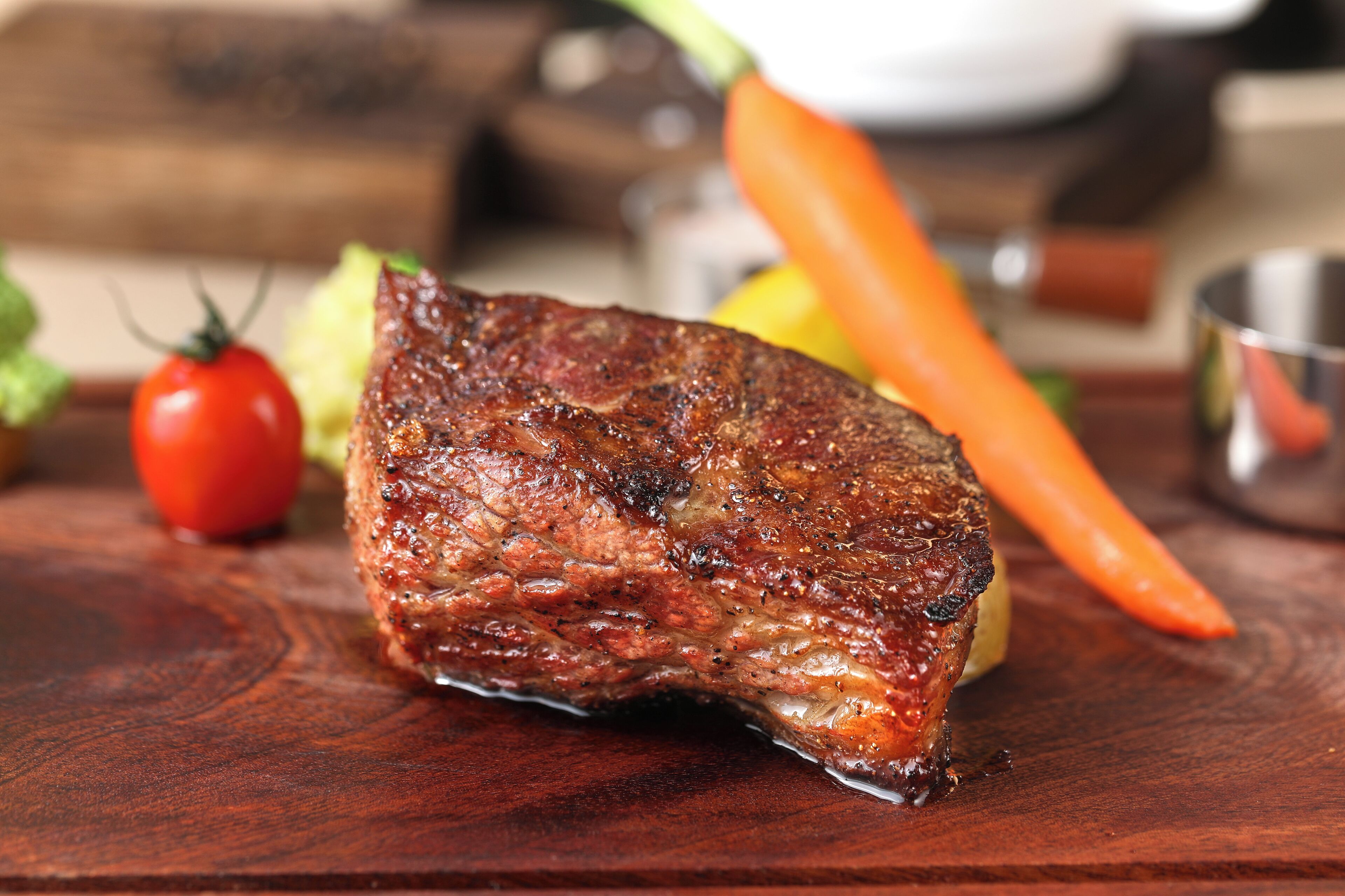 Bife sobre tábua de madeira, com vegetais ao fundo.