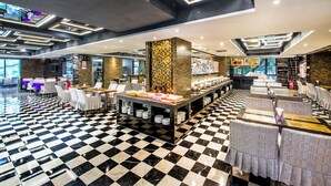 Un amplio vestíbulo de hotel con piso a cuadros, varias áreas de descanso y una mesa de buffet central.
