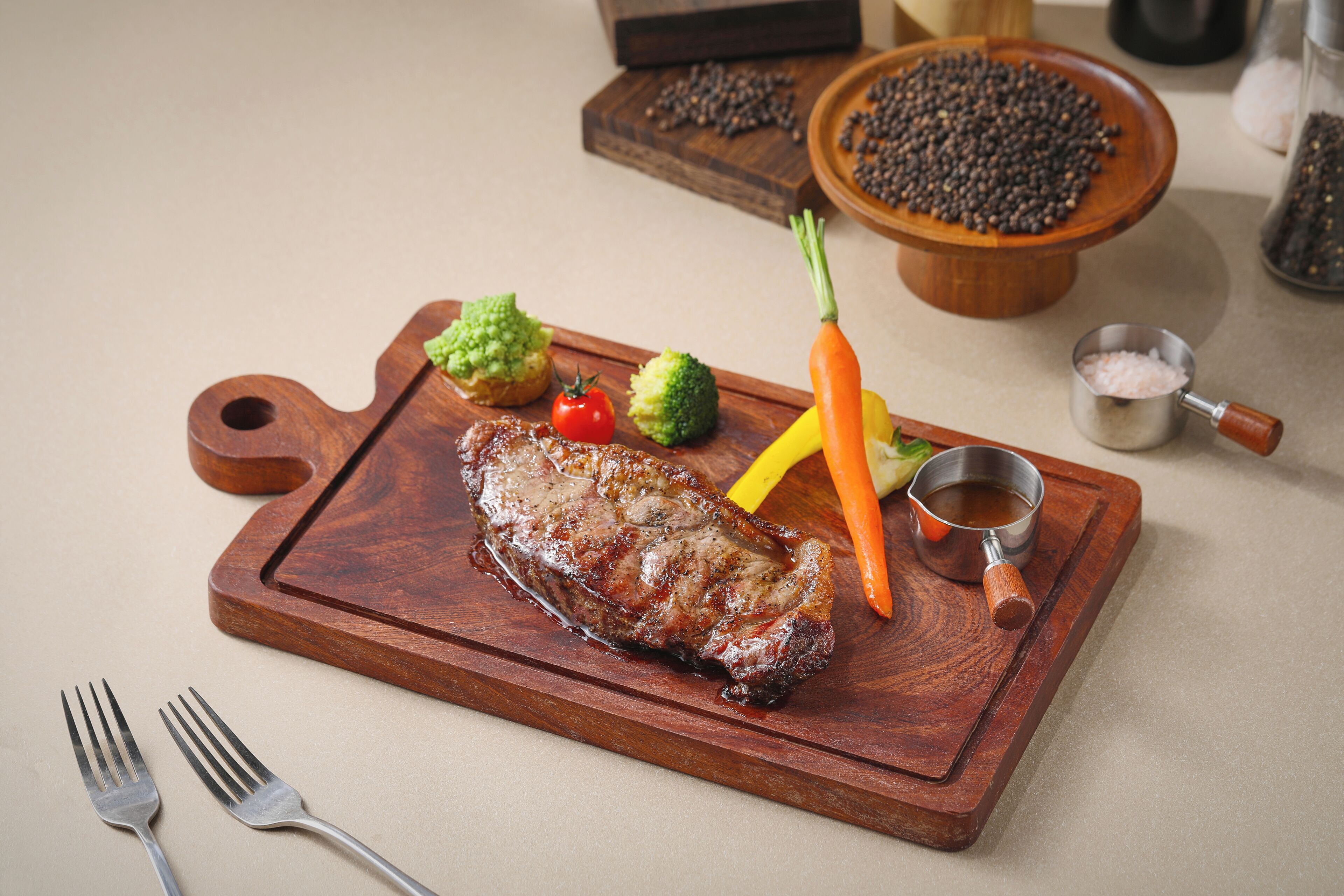 A wooden cutting board with a steak, vegetables, and condiments.