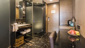 Un baño moderno con cabina de ducha de vidrio, lavabo con encimera de mármol y tocador con superficie de vidrio y frutero.