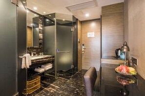 A modern bathroom with a glass shower enclosure, a vanity with a marble countertop, and a bowl of fruit on the counter. - La Perle International Hotel (Guangzhou)