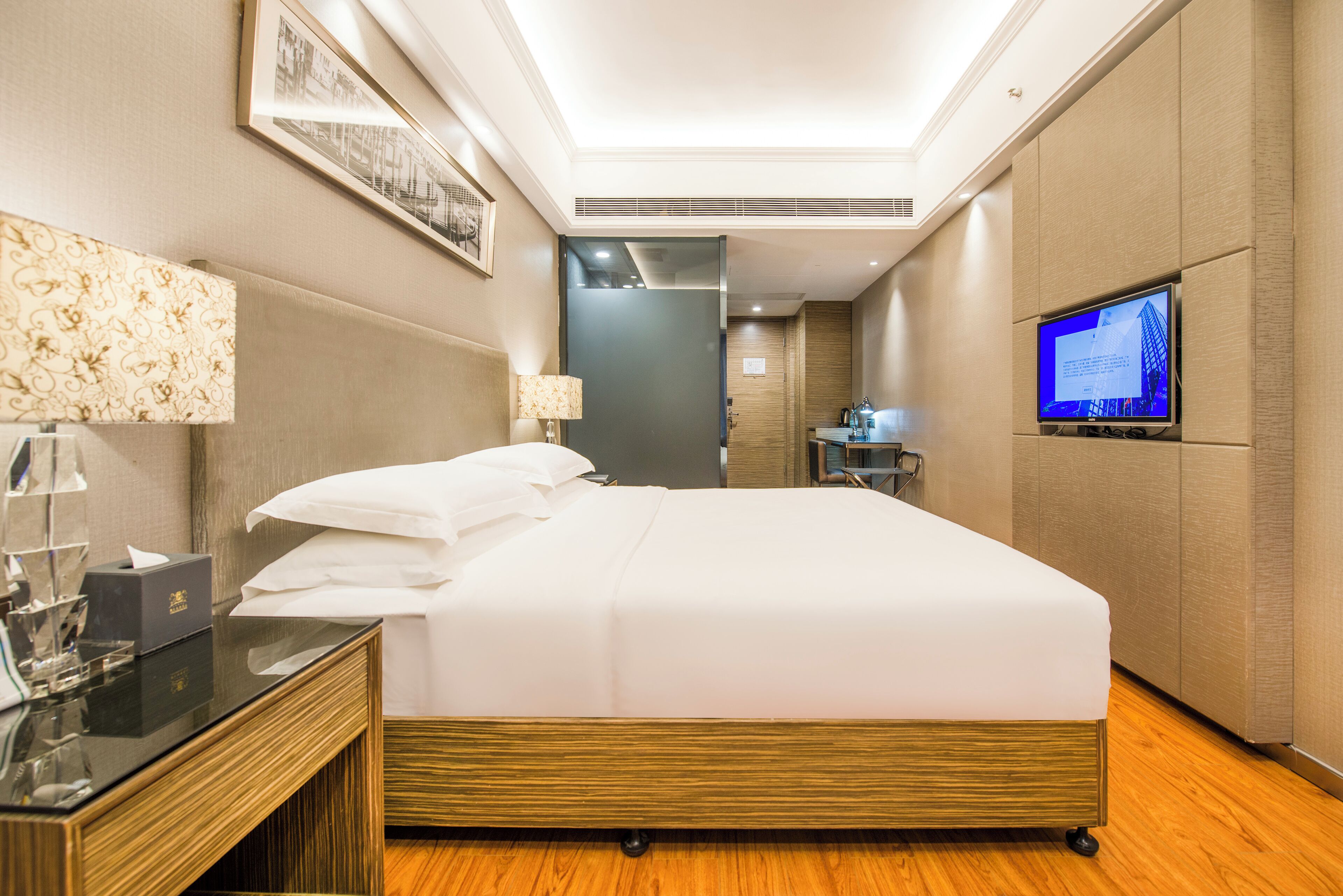 A hotel room with a large bed, a desk with a lamp, a television, and a bathroom visible through an open door.
