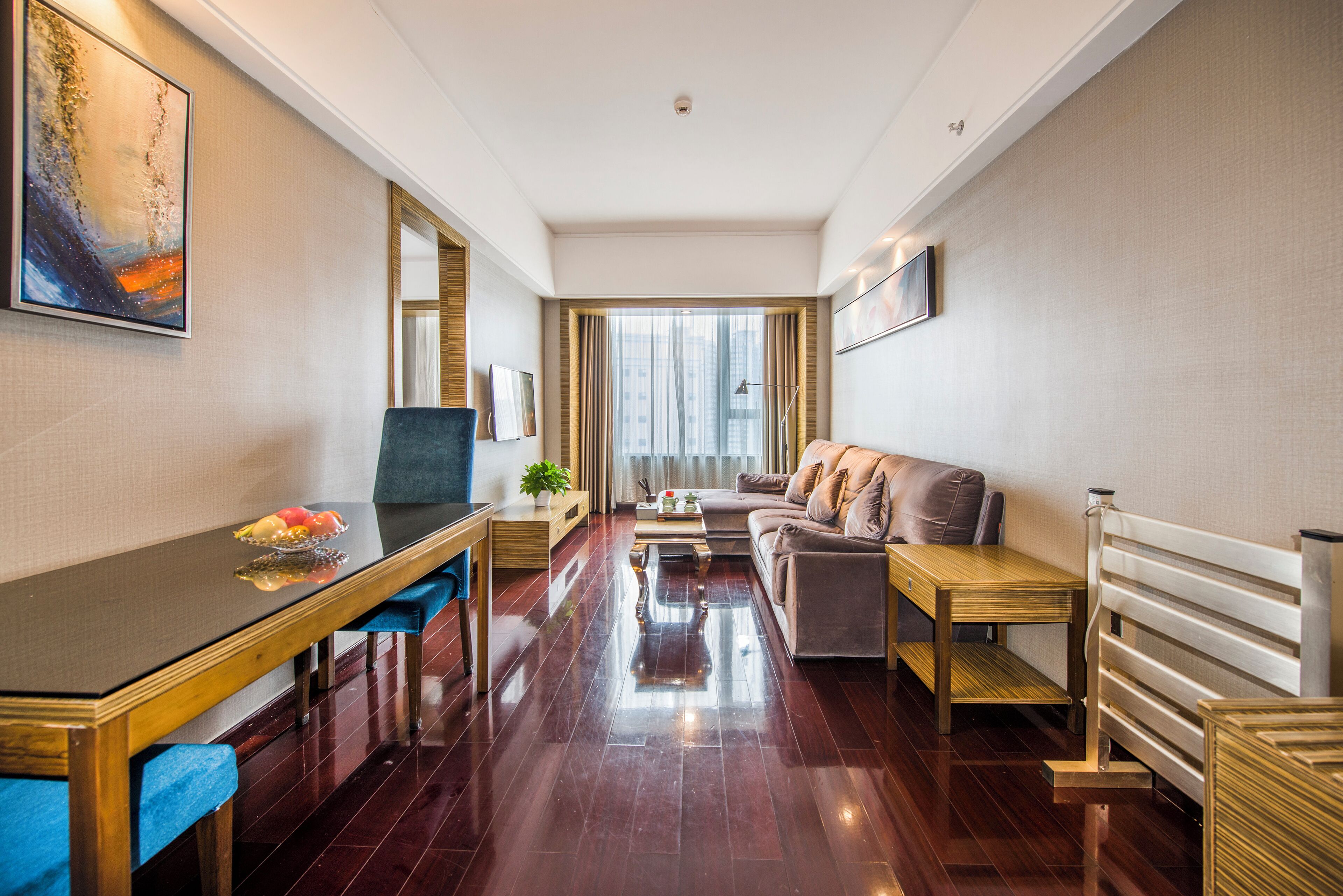Una habitación de hotel moderna con una mesa de comedor de madera, sillas tapizadas en azul, un sofá y un ventanal con cortinas.