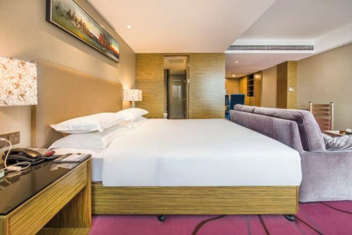 A hotel room with a large bed, a desk with a telephone, and a door leading to a bathroom.