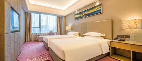 A hotel room with two beds, a desk, a lamp, a painting, and a large window with curtains.