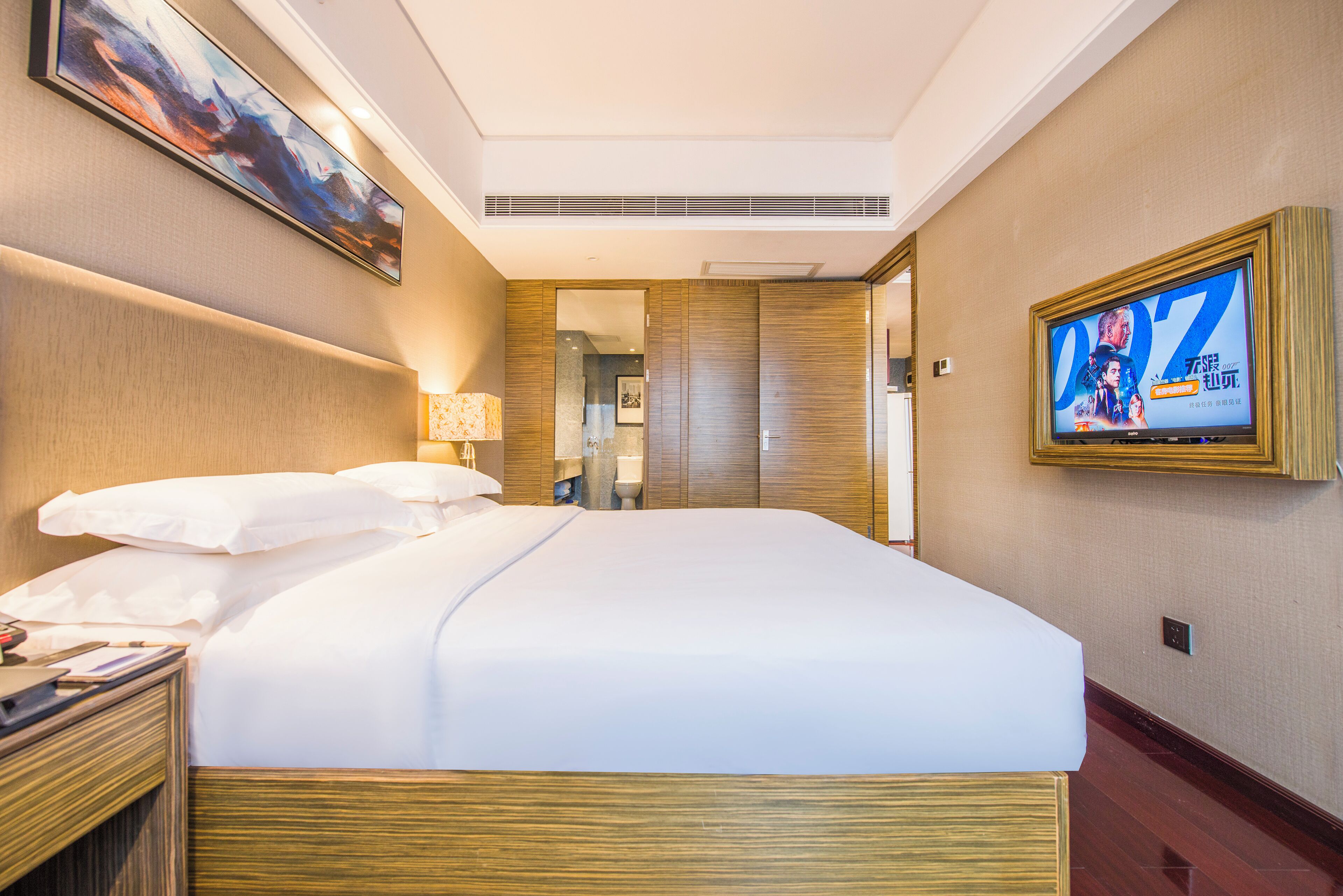 Habitación de hotel con una cama grande, un televisor en la pared y un cuadro sobre la cama.
