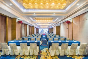 Una sala conferenze con file di tavoli e sedie, una moquette decorata e un lampadario.
