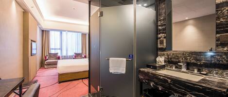 A hotel room with a bed, a shower, a vanity with a mirror, and a desk.
