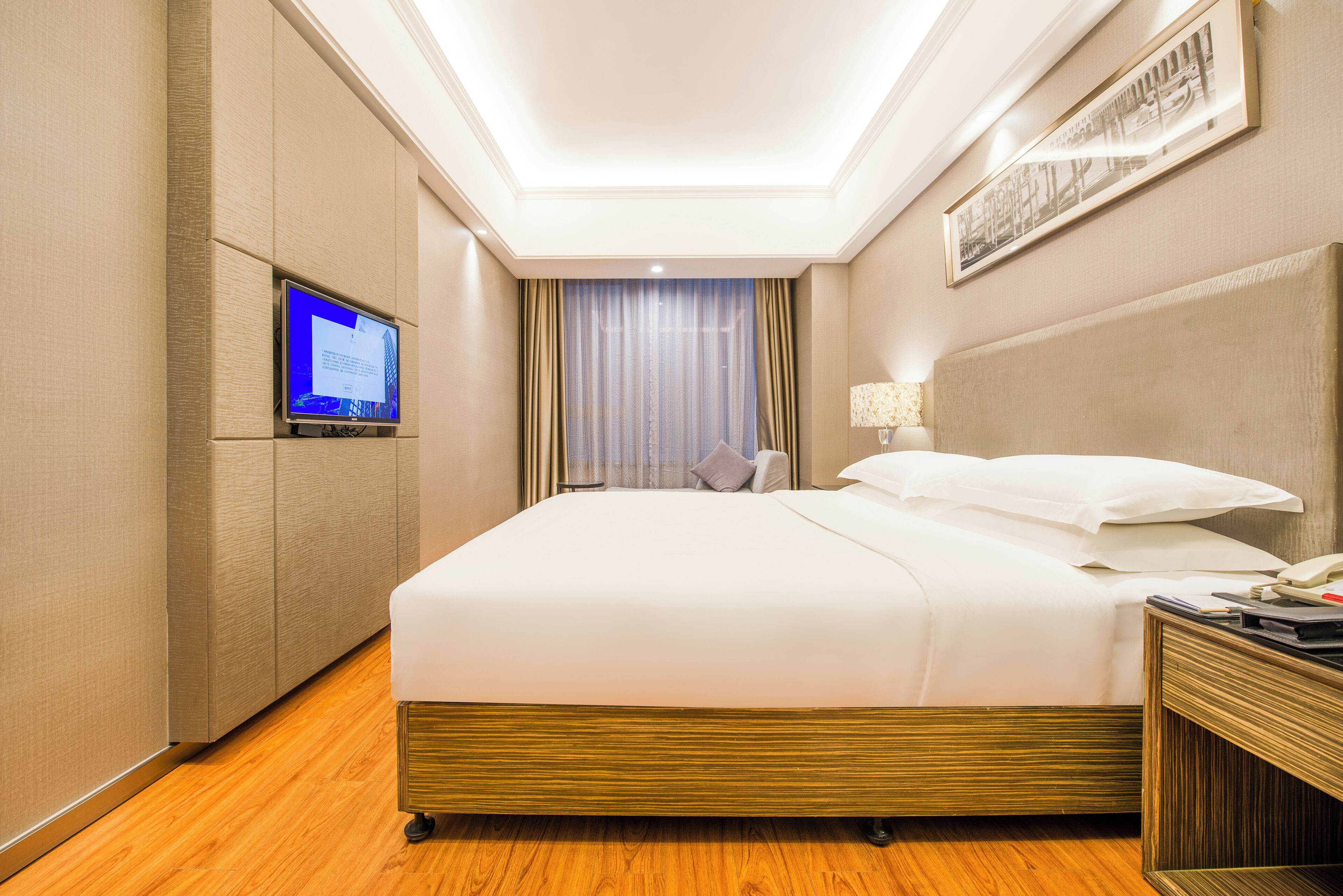Une chambre d’hôtel avec un grand lit, un téléviseur fixé au mur, une table de chevet et une fenêtre avec des rideaux.