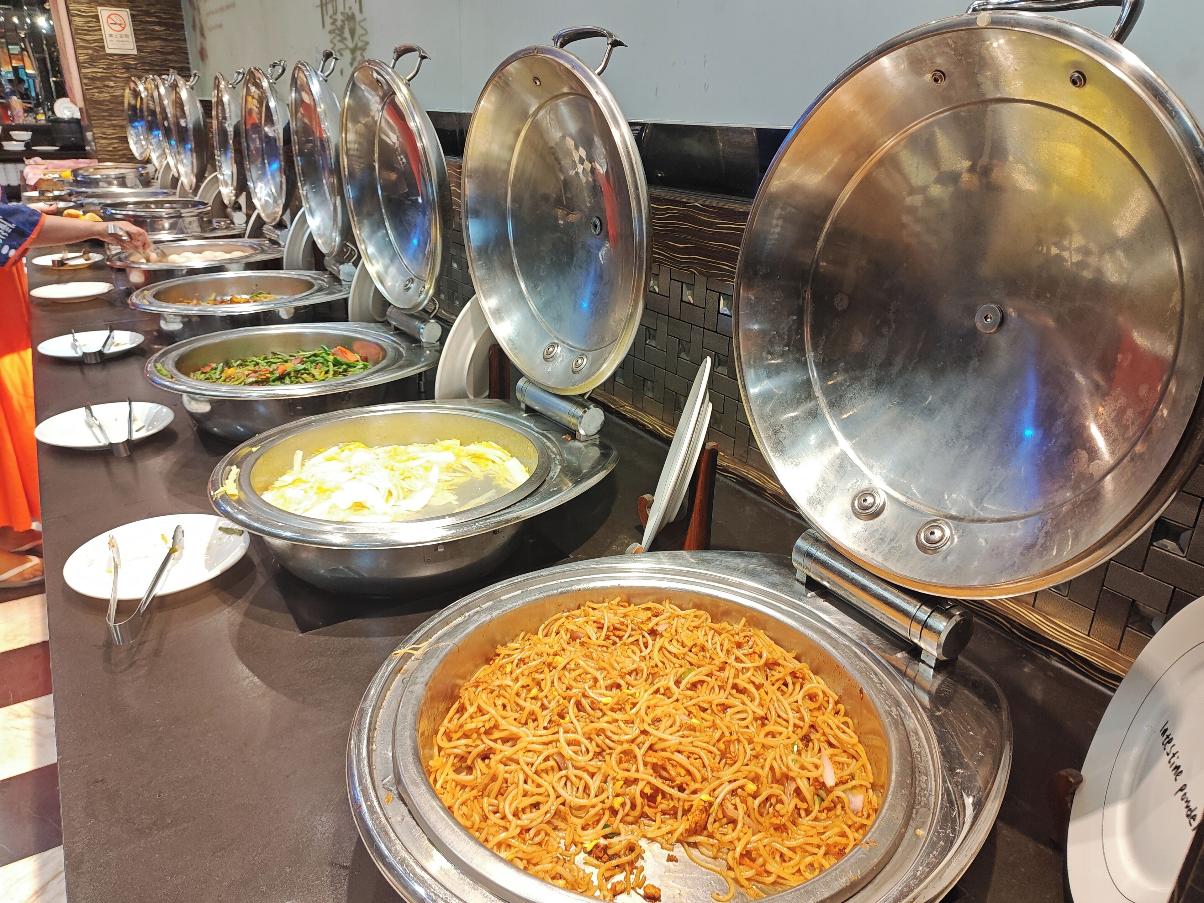 A buffet setup with various food items in metal serving dishes, including noodles and vegetables.