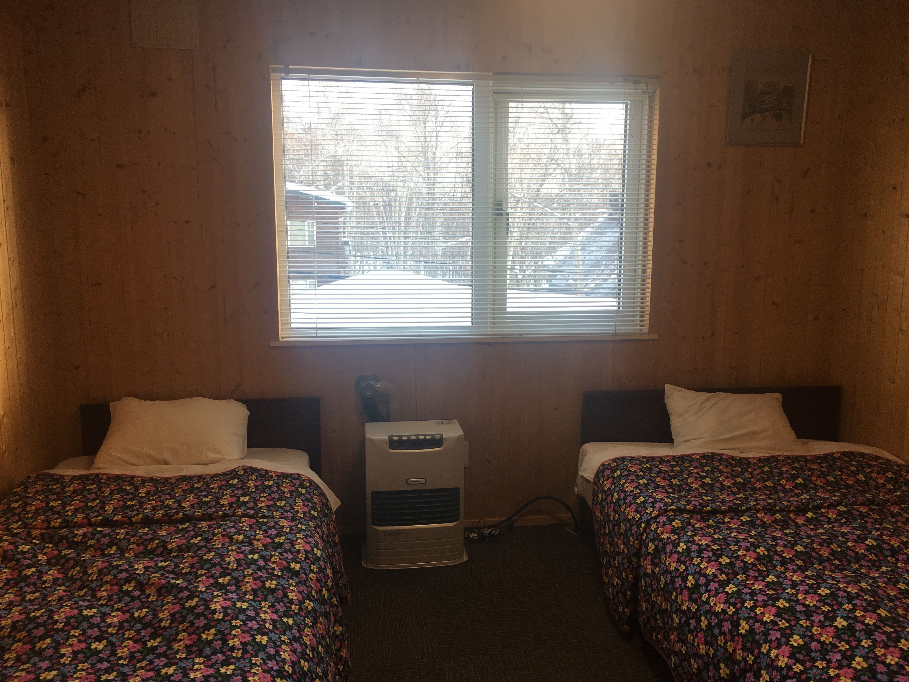 Una habitación con dos camas, un calentador y una ventana con persianas.