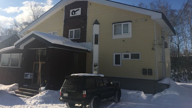 A two-story building with a garage, a Lexus SUV parked in front, and snow on the ground. - Pension Fryingpan (Niseko)