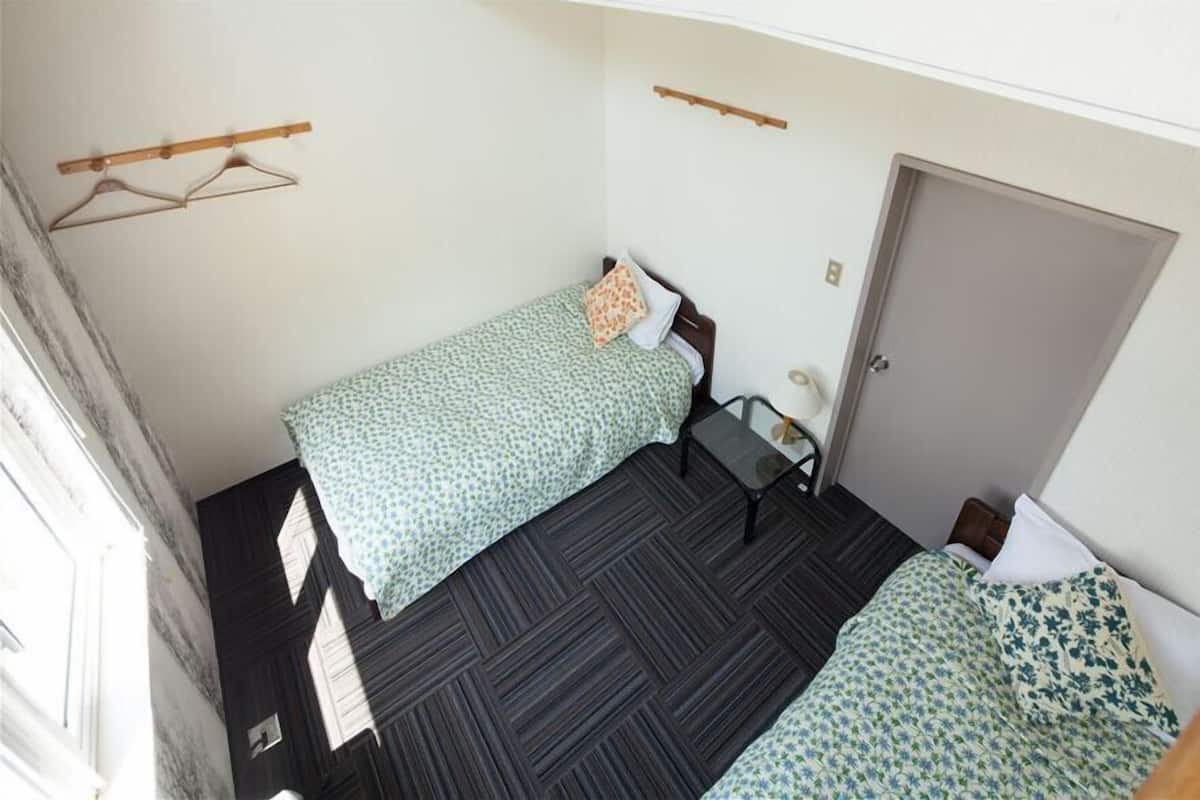 A small, compact room with two single beds, a small table, and a wardrobe.