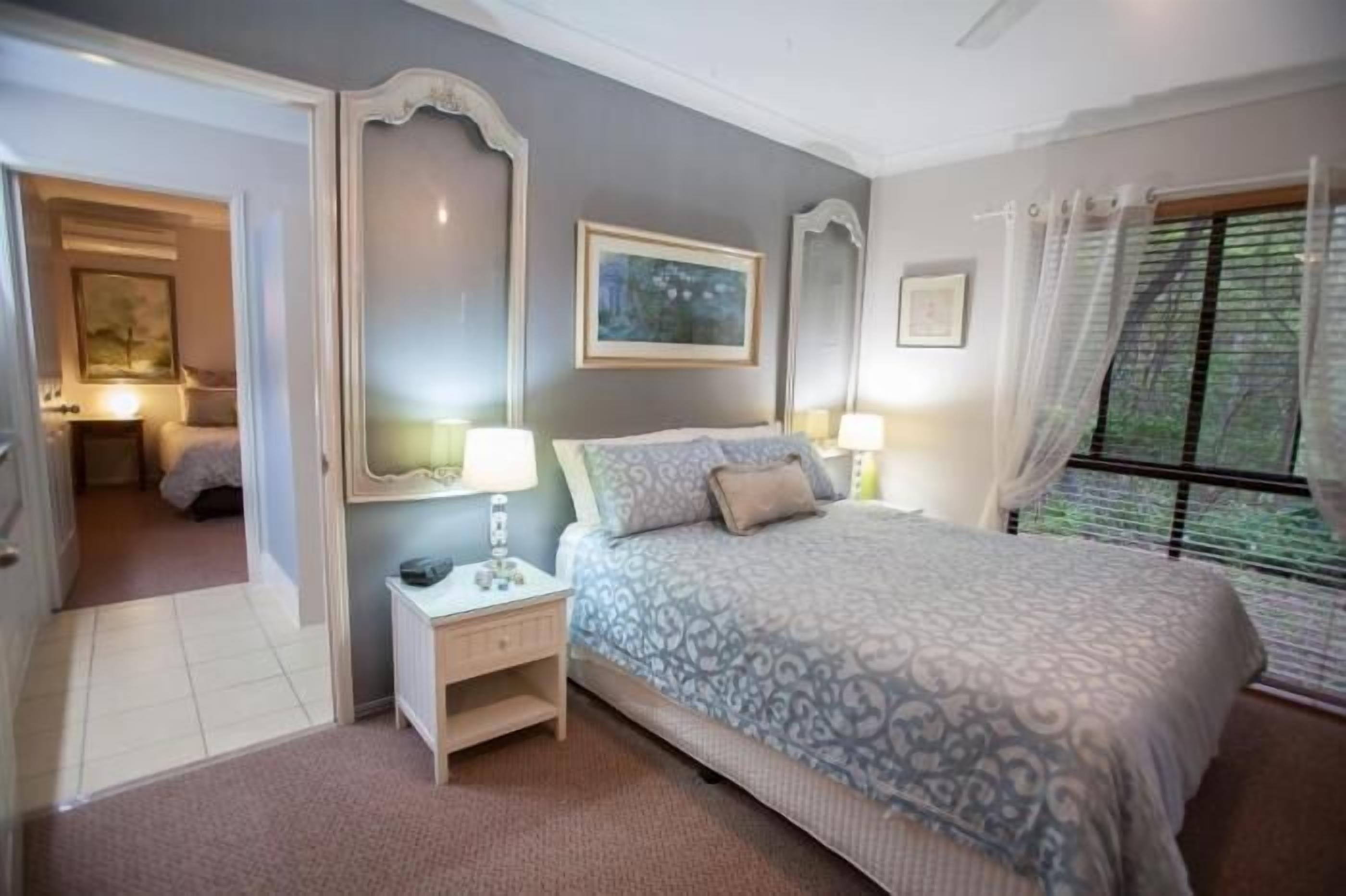 A bedroom with a large bed, a nightstand, a mirror, and a window with curtains.