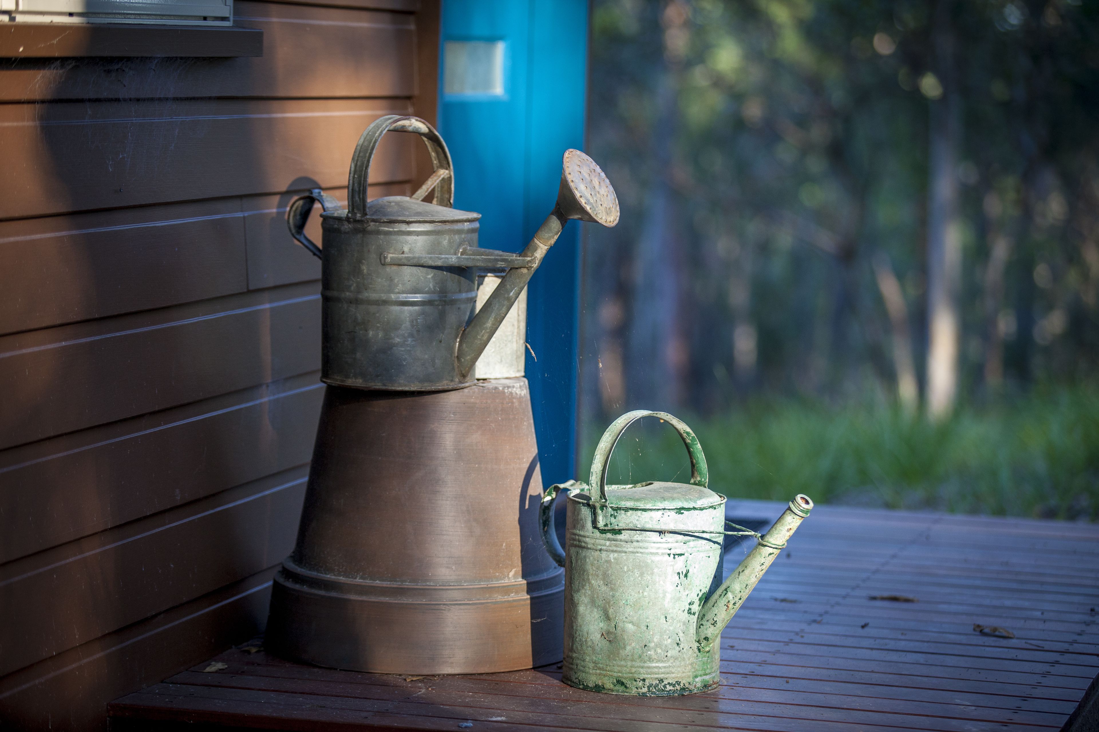 Two metal watering cans on a wooden deck.