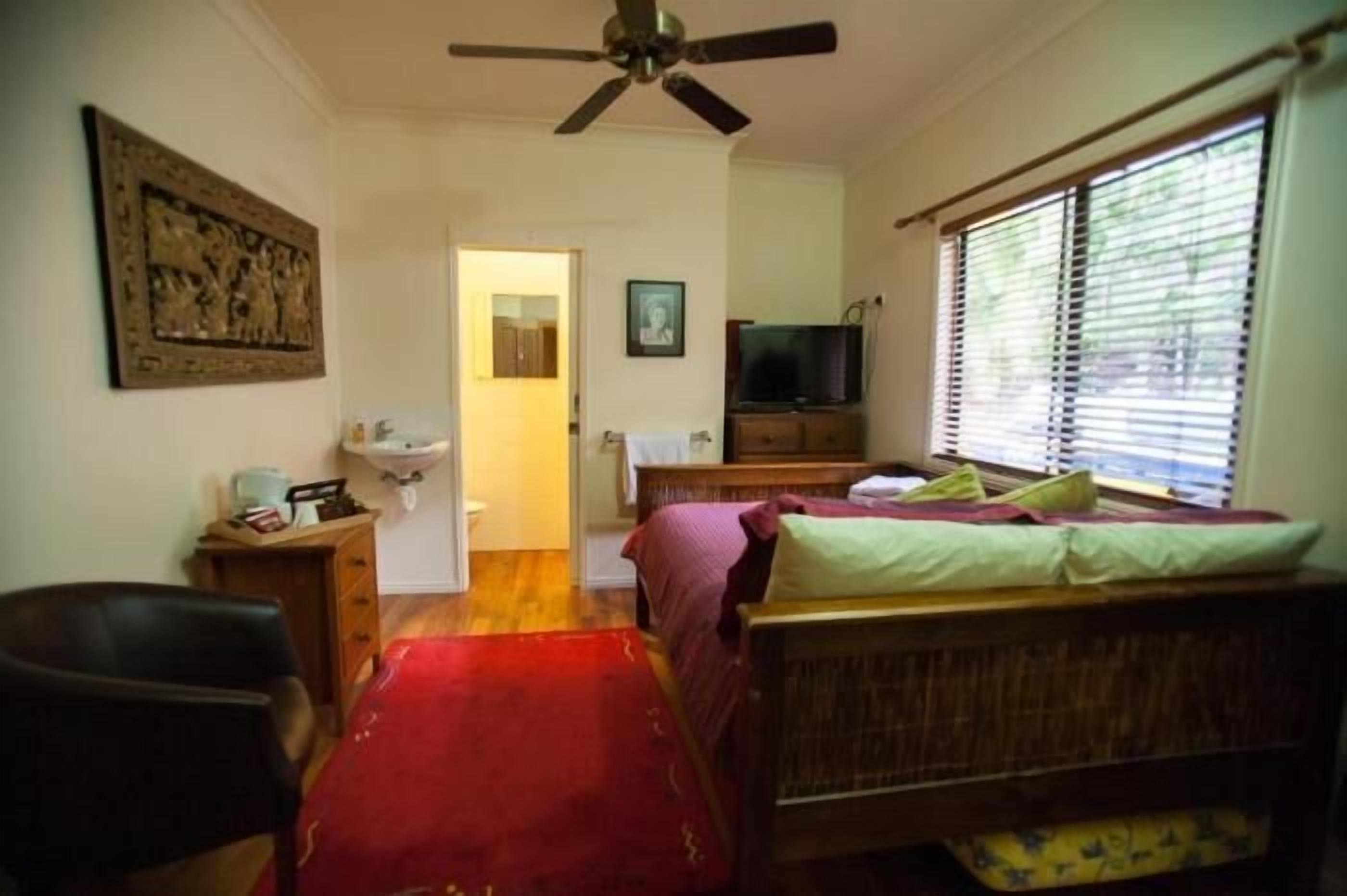 A bedroom with a bed, a desk, a chair, a television, and a window with blinds.
