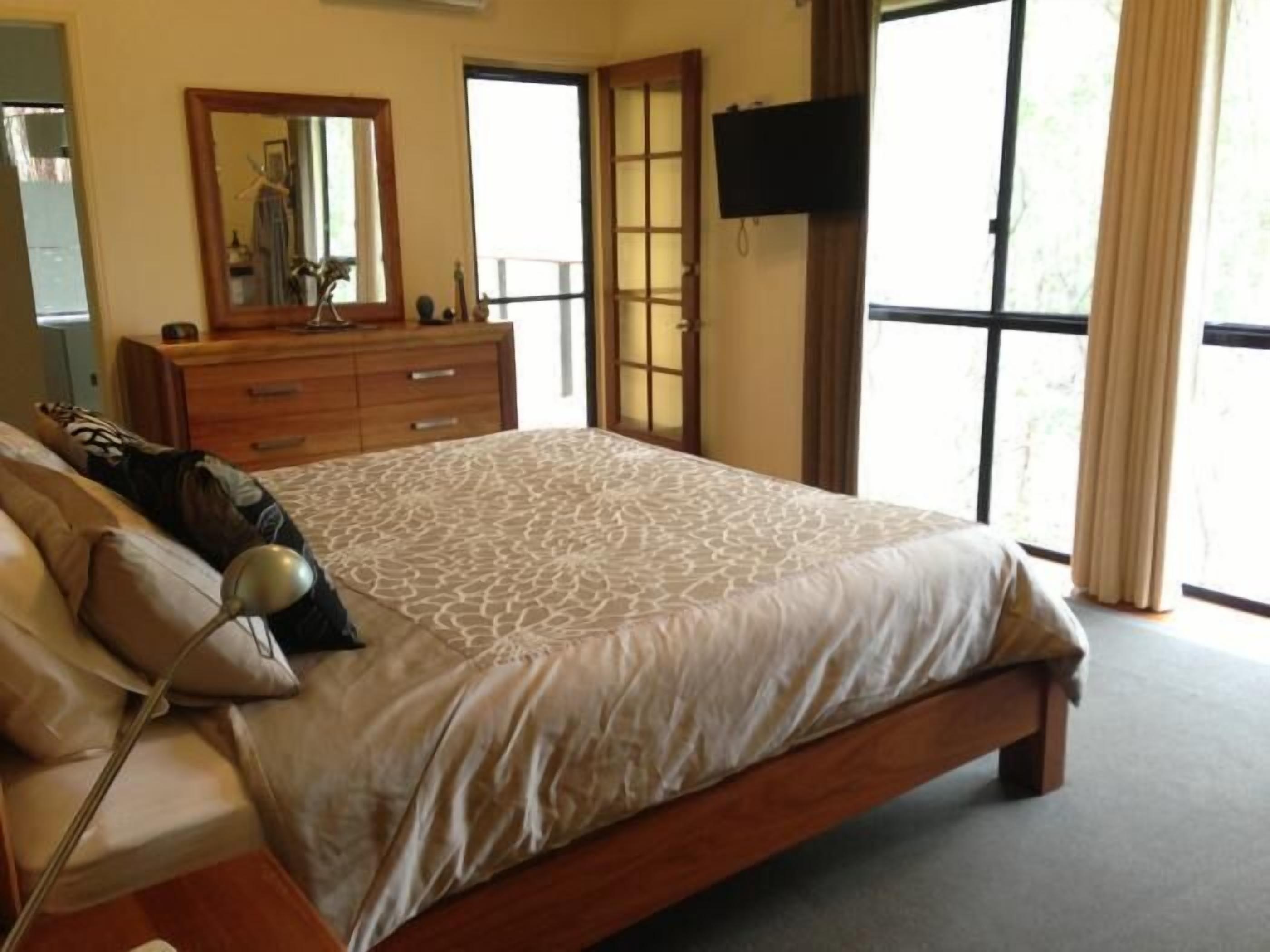 A bedroom with a large bed, a dresser, a mirror, a TV, and a sliding glass door leading to a balcony.