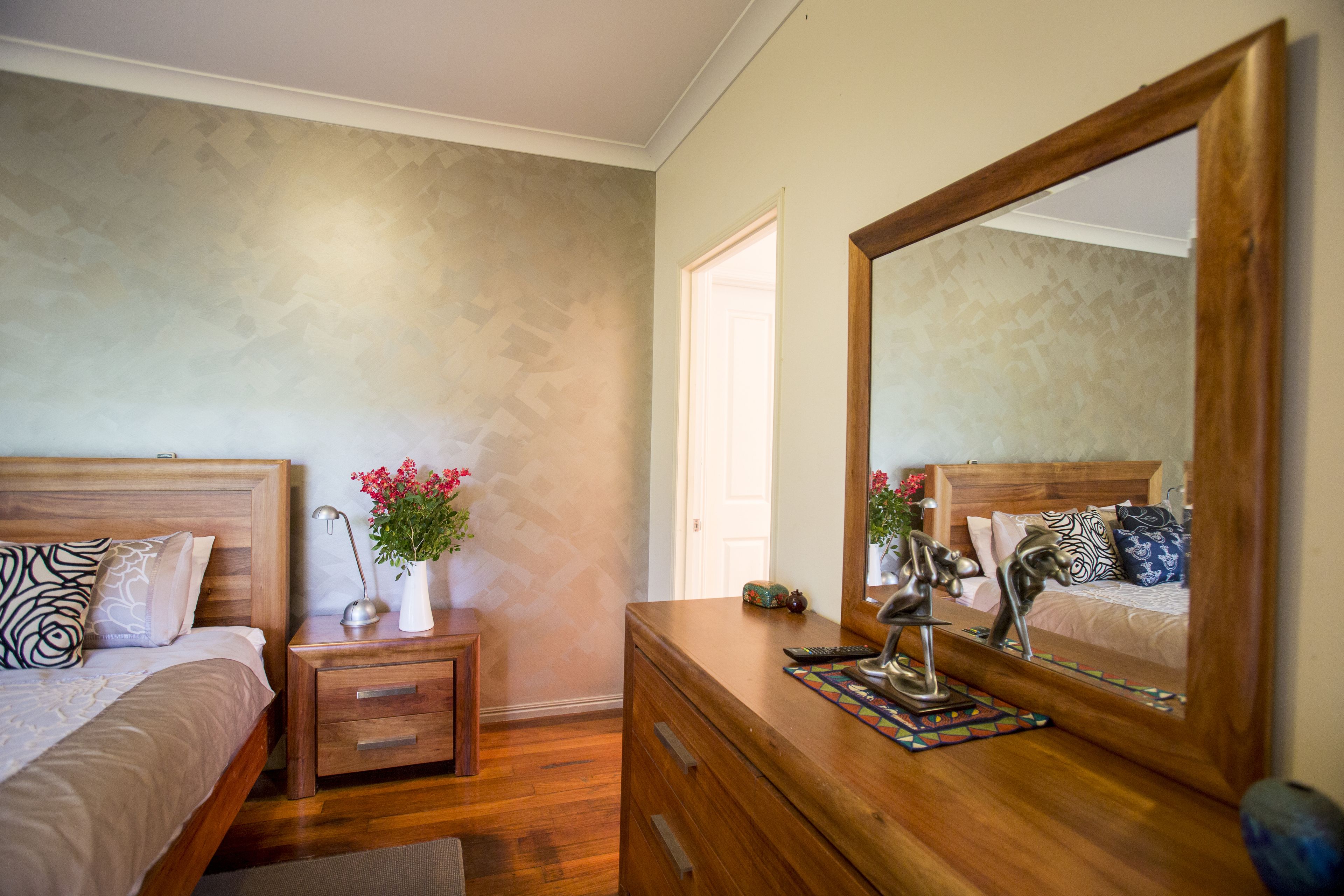 Un dormitorio con cama de madera, mesita de noche, cómoda y un espejo grande.