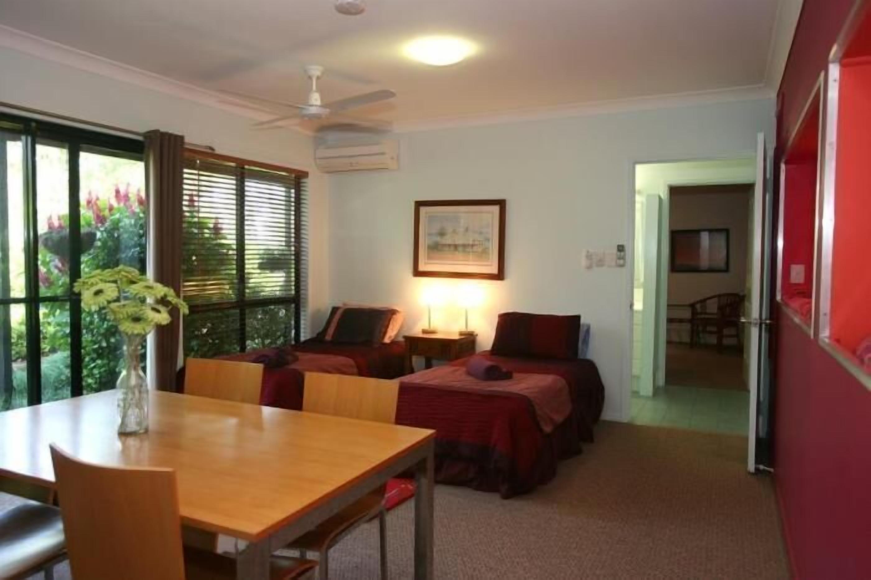 Habitación de hotel con dos camas, una mesa de comedor y una ventana con persianas.