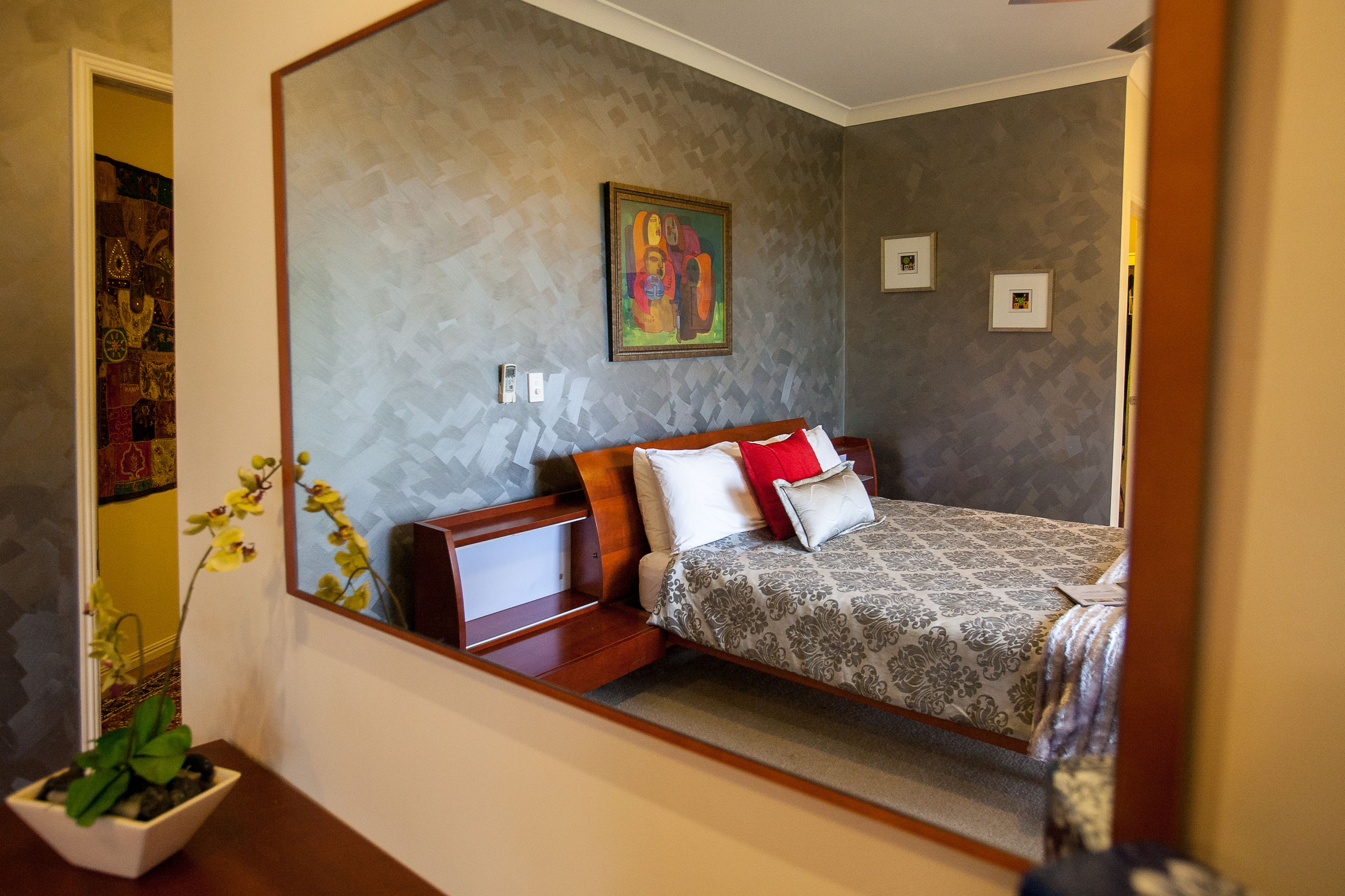A bedroom with a bed, a nightstand, a potted plant, and a painting on the wall.
