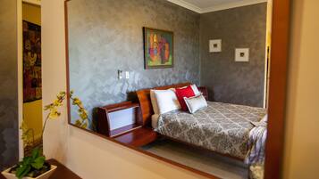A bedroom with a bed, a nightstand, a potted plant, and a painting on the wall.